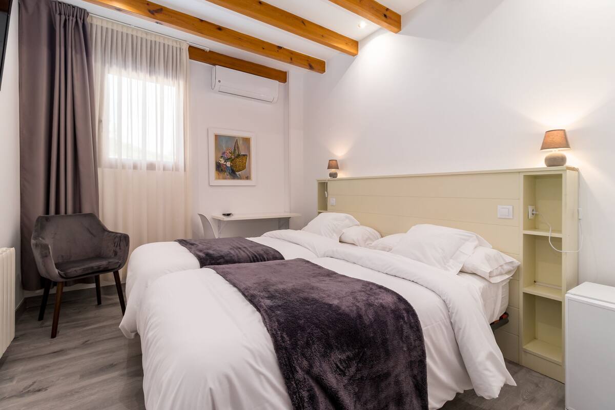 Een hotelkamer met twee bedden, een bureau, een stoel en een nachtkastje met een lamp.