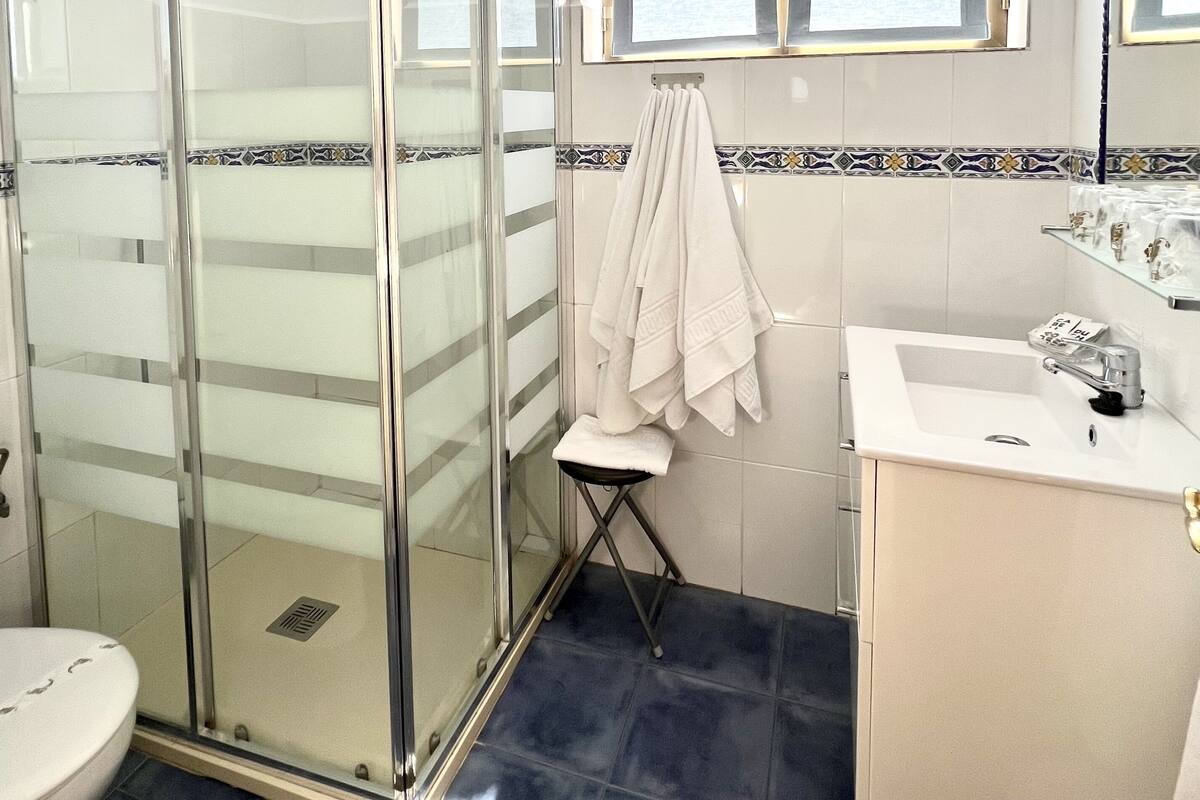 Een badkamer met een douchecabine van glas, een witte wastafel en een raam boven de spiegel.