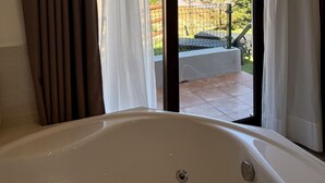 A bathroom with a bathtub, a view of a garden through a sliding glass door, and a view of a pool area. - Hotel Sanmar (Alfoz de Lloredo)