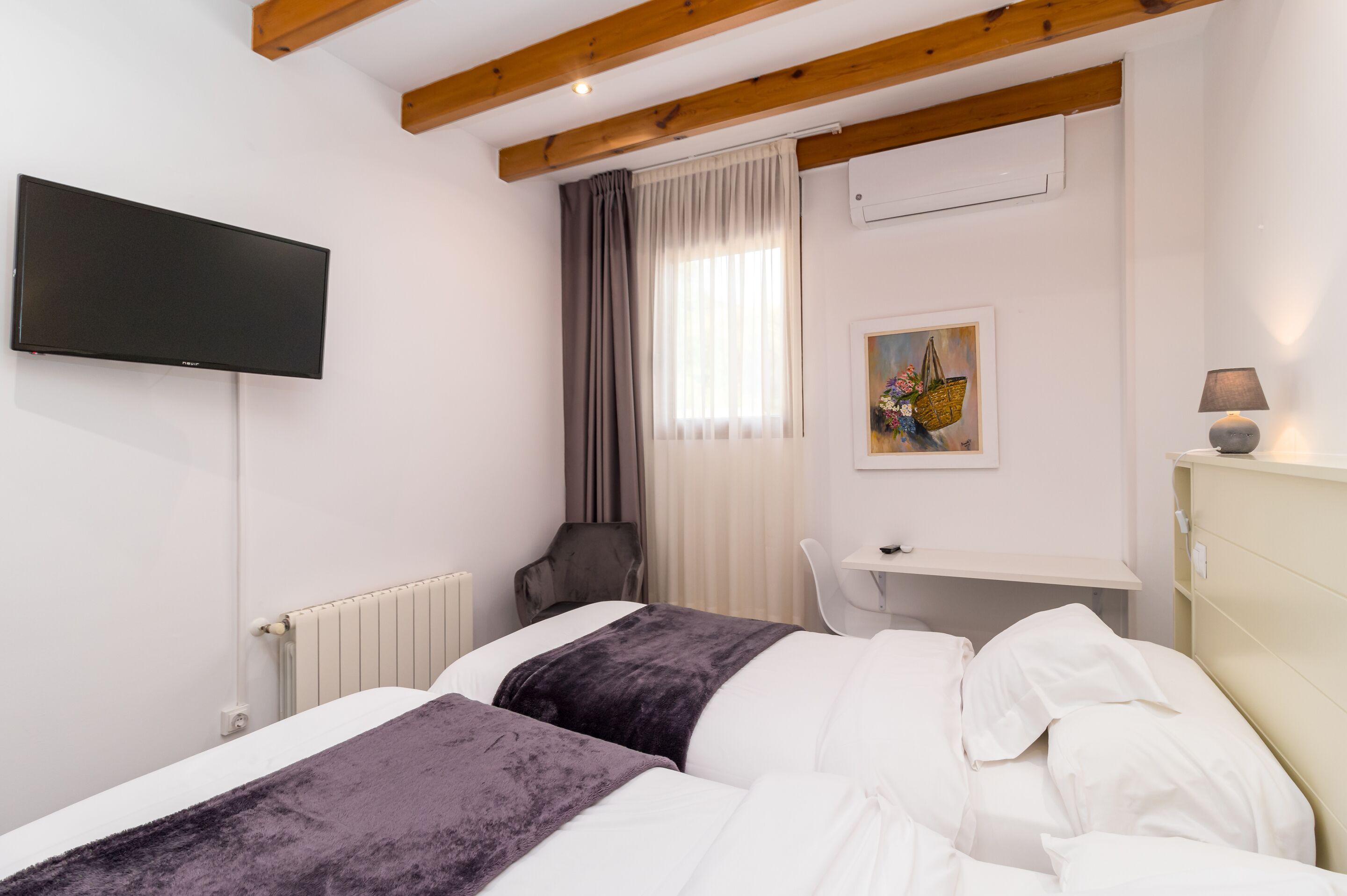 Una camera d'albergo con due letti, una scrivania, una sedia, un televisore e un quadro appeso al muro.