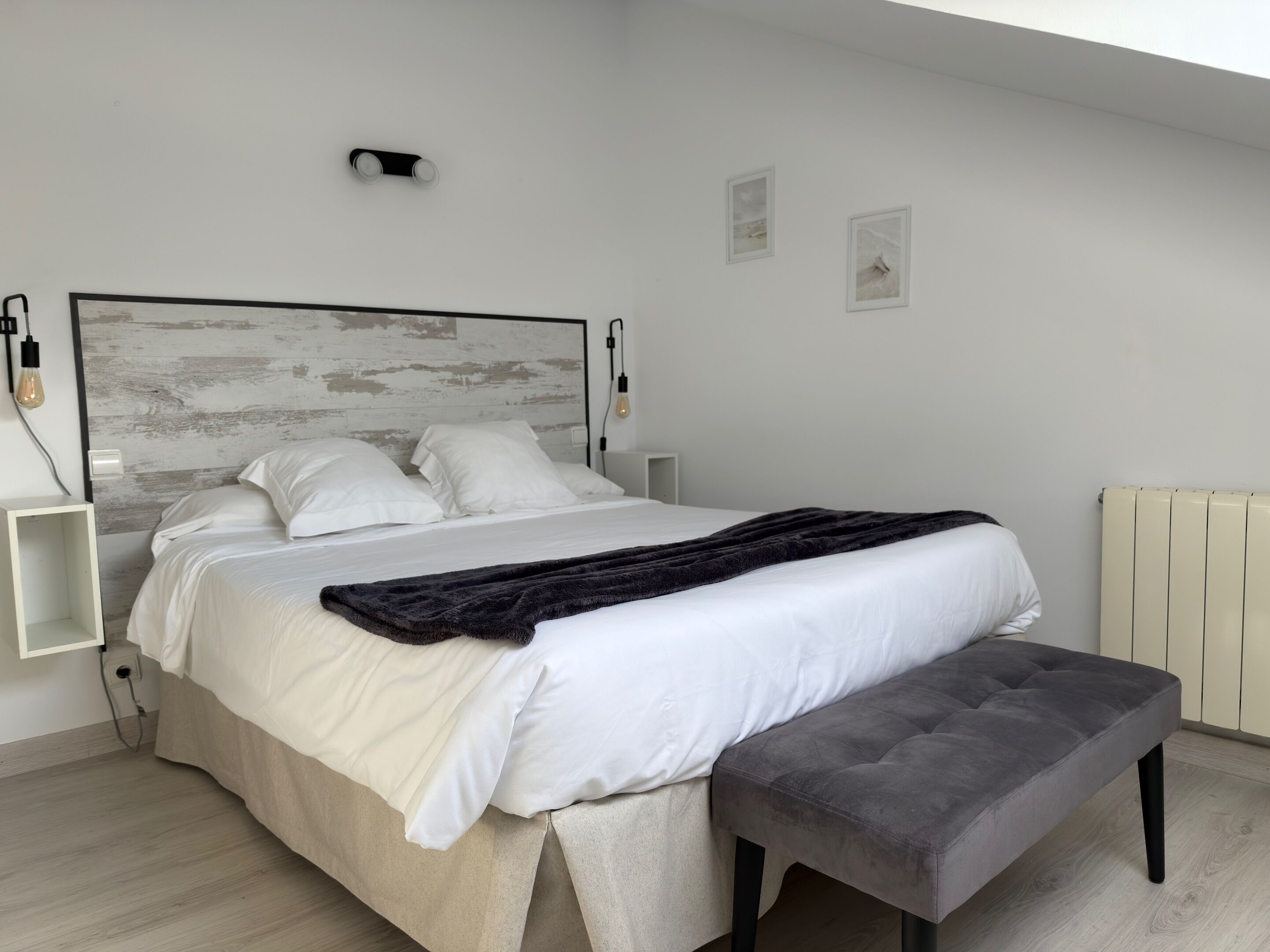 Un dormitorio moderno con cama, mesitas de noche, un banco y un radiador.