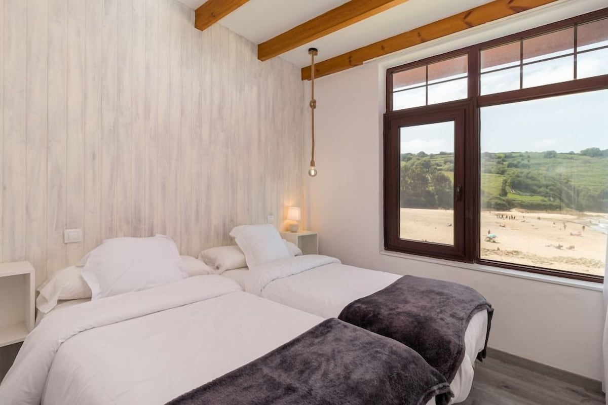 Un dormitorio con dos camas, un ventanal con vistas a la playa y vigas de madera en el techo.