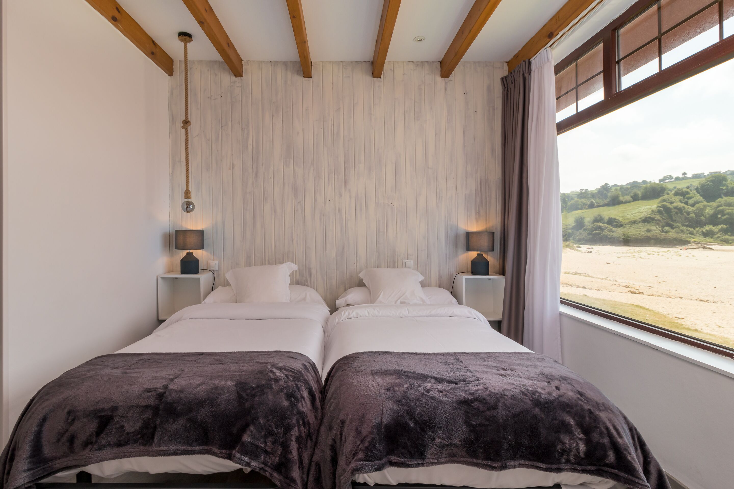 Habitación doble con vista a la playa, vigas de madera en el techo y lámparas de noche.