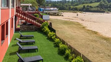 Un hotel con fachada roja, una escalera que lleva a una terraza y vista al mar.