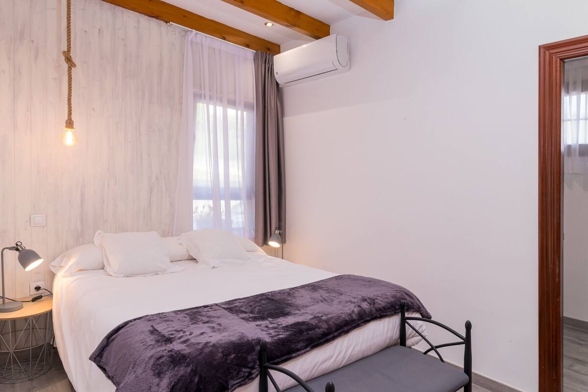 Een slaapkamer met een bed, bedlampje en een raam met gordijnen.