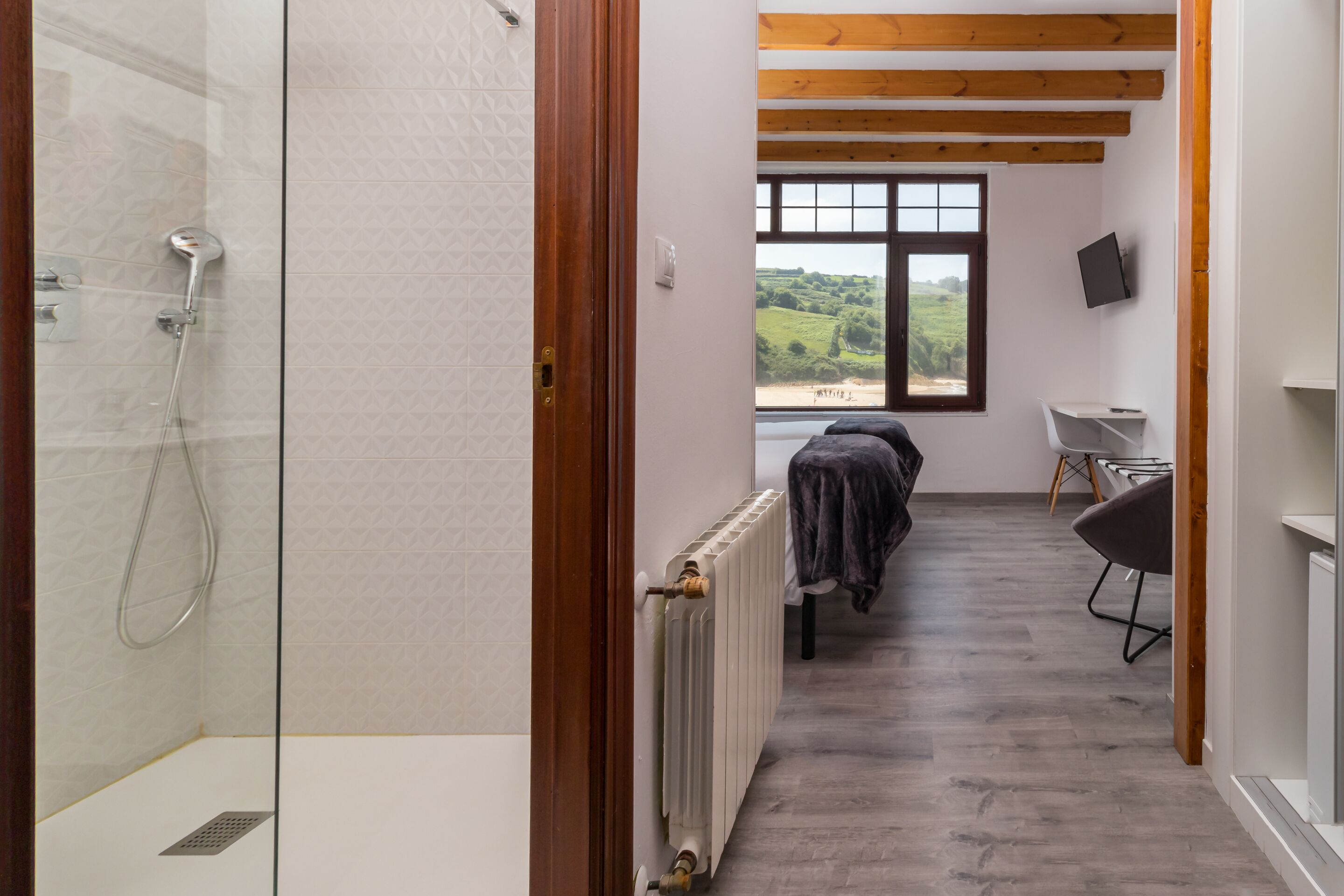 A modern bathroom with a glass shower enclosure, a radiator, and a view of a green landscape through a window.