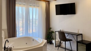 A modern bathroom with a freestanding bathtub, a desk with a chair, and a flat-screen TV mounted on the wall. - Hotel Sanmar (Alfoz de Lloredo)
