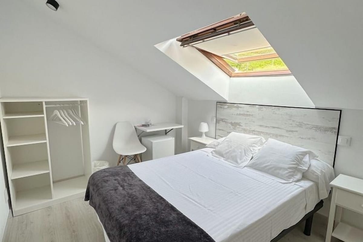 Un dormitorio con tragaluz, una cama, un escritorio y un armario.