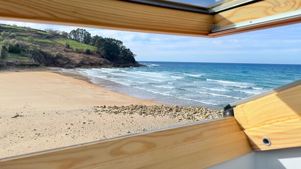 A beach view through a window with a wooden frame. - Hotel Sanmar (Alfoz de Lloredo)