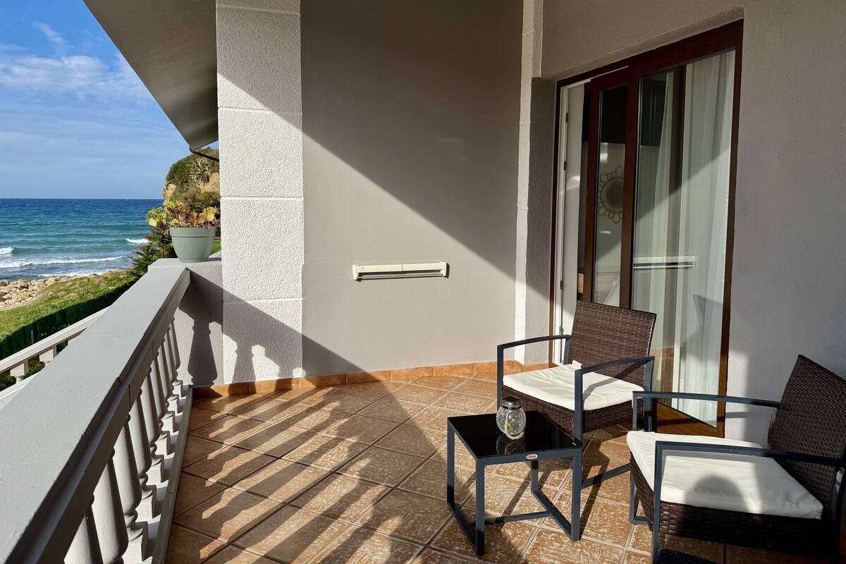Een balkon met uitzicht op de oceaan, een stoel, een tafeltje en een bloempot.