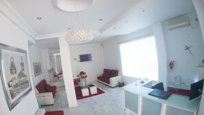 Een moderne woonkamer met een witte bank, rode kussens, een glazen salontafel en een kroonluchter.