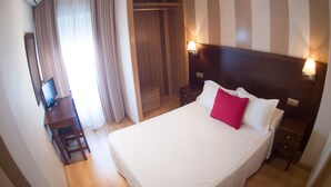 Een hotelkamer met een groot bed, een houten garderobe, een bureau met stoel en een televisie.