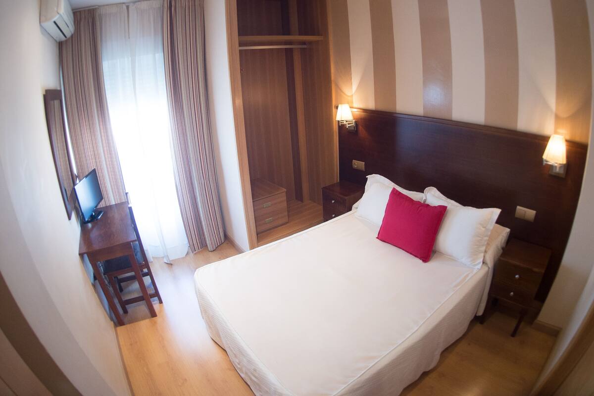 Une chambre d’hôtel avec un grand lit, une armoire en bois, un bureau avec une chaise et une télévision.