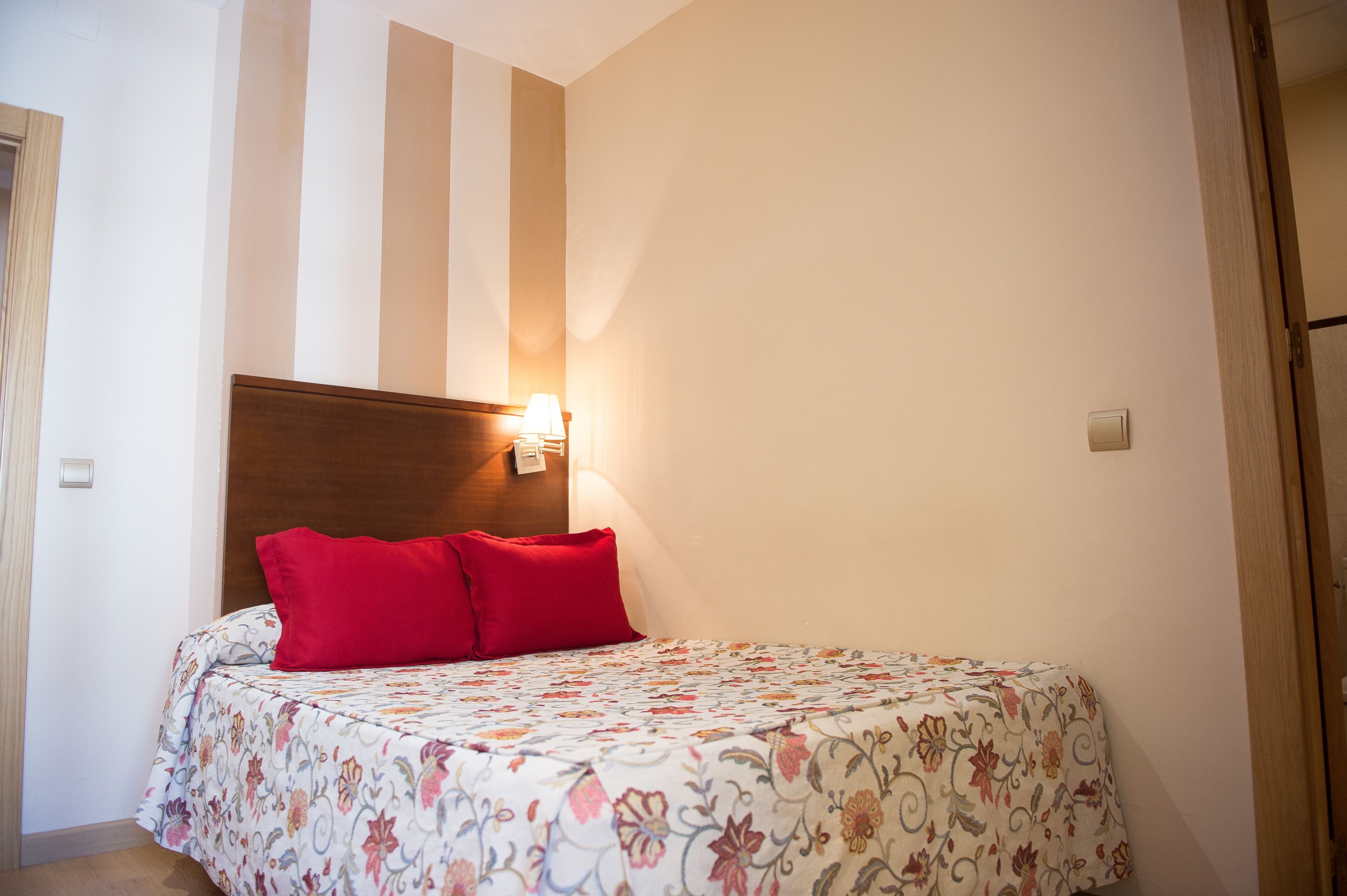 Un dormitorio con cama, mesita de noche, lámpara y luz empotrada en la pared.