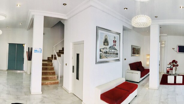 Een moderne hotel lobby met een trap, zitgedeeltes in rood en wit, en een kroonluchter.