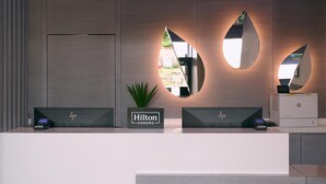 A modern hotel reception desk with two monitors, a plant, and a printer. - Spark by Hilton Luton (Luton)