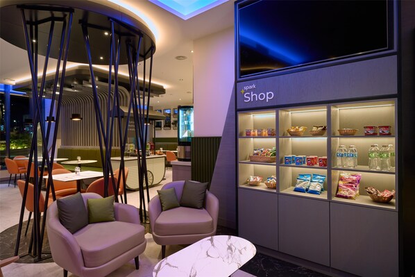 A modern interior with seating, a marble table, and a shop with various products. - Spark by Hilton Luton (Luton)