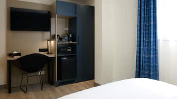 A hotel room with a bed, a desk with a chair, a TV, a mini-fridge, and a wardrobe.
