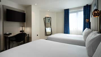 Une chambre d’hôtel avec deux lits, un bureau, une chaise, une télévision, un miroir et une fenêtre avec des rideaux.