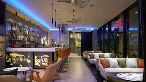 A modern bar area with a long counter, multiple shelves of bottles, and a seating area with sofas and chairs. - Spark by Hilton Luton (Luton)