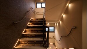 A staircase with wooden steps and a metal railing, illuminated by wall-mounted lights. - Spark by Hilton Luton (Luton)
