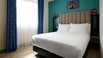 Una habitación de hotel moderna con una cama grande, una mesita de noche, una lámpara de pared y un cuadro.