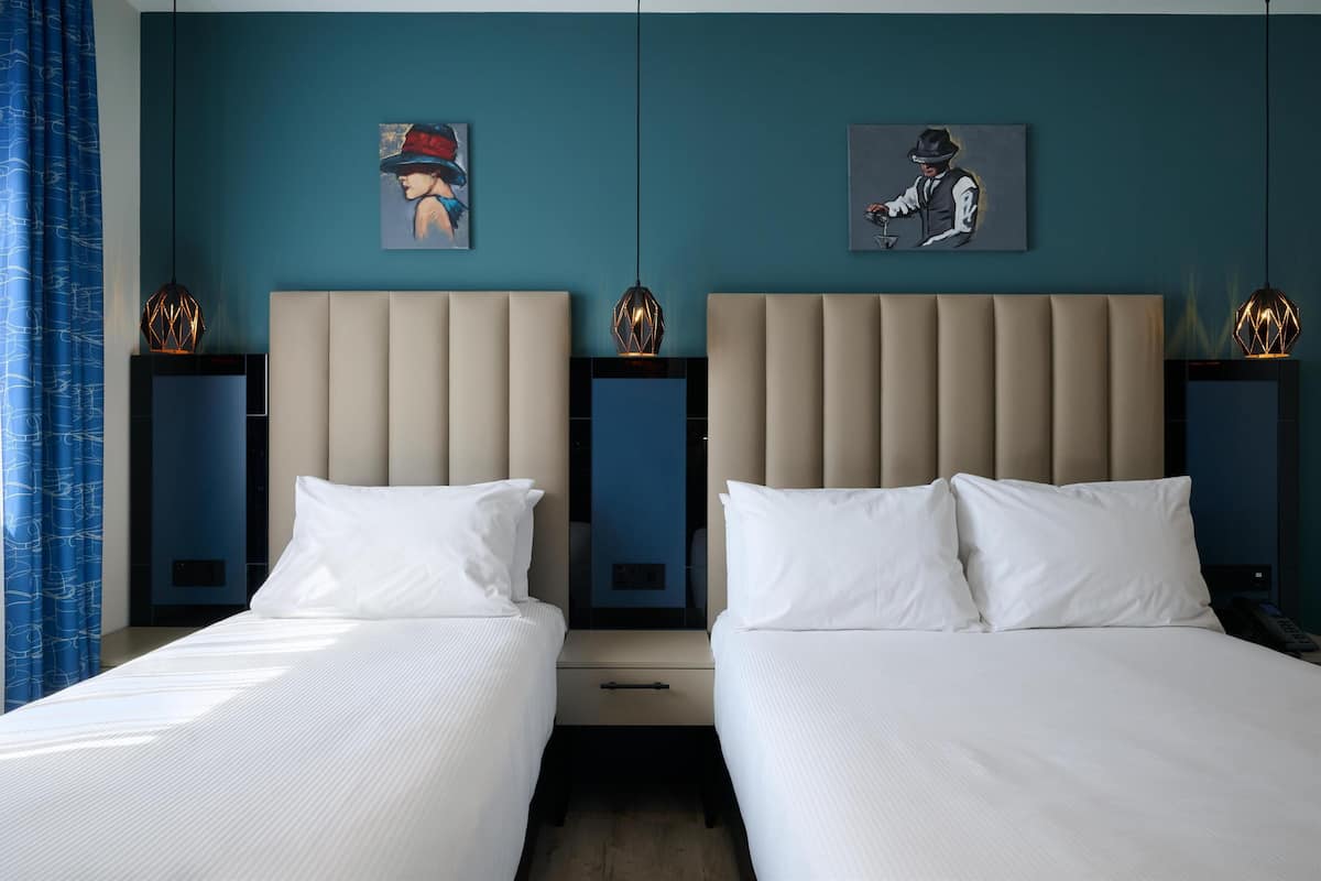 A hotel room with two beds, a blue wall, and artwork.