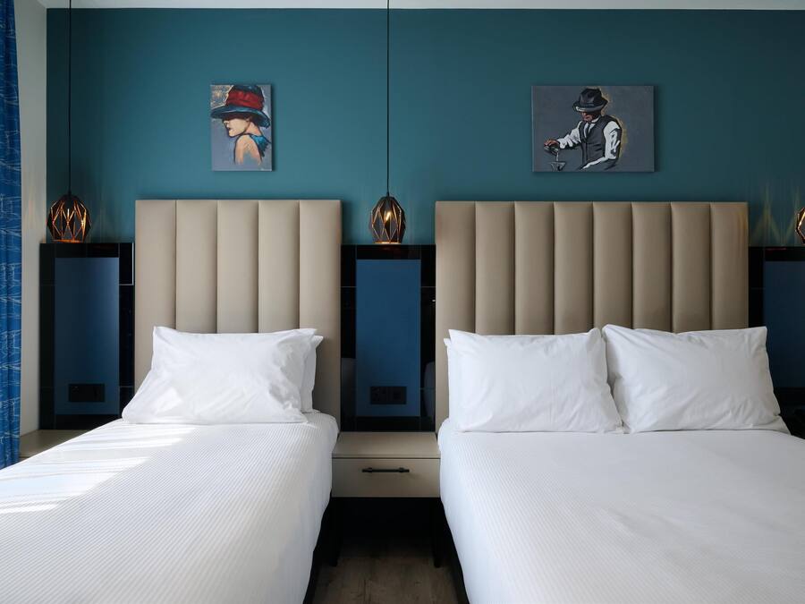 Hotellihuone, jossa on kaksi sänkyä, sininen seinä ja taideteoksia.