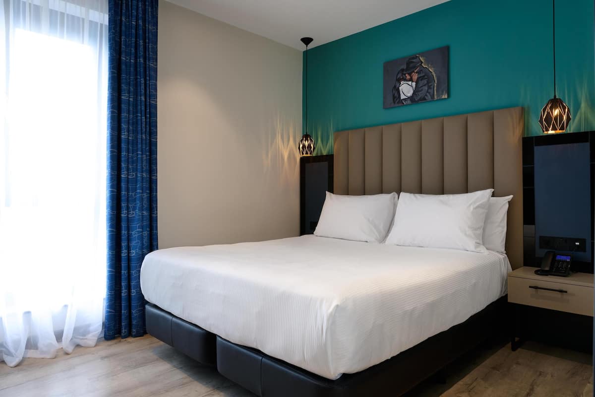 A modern hotel room with a large bed, a nightstand with a phone, and a painting on the wall.