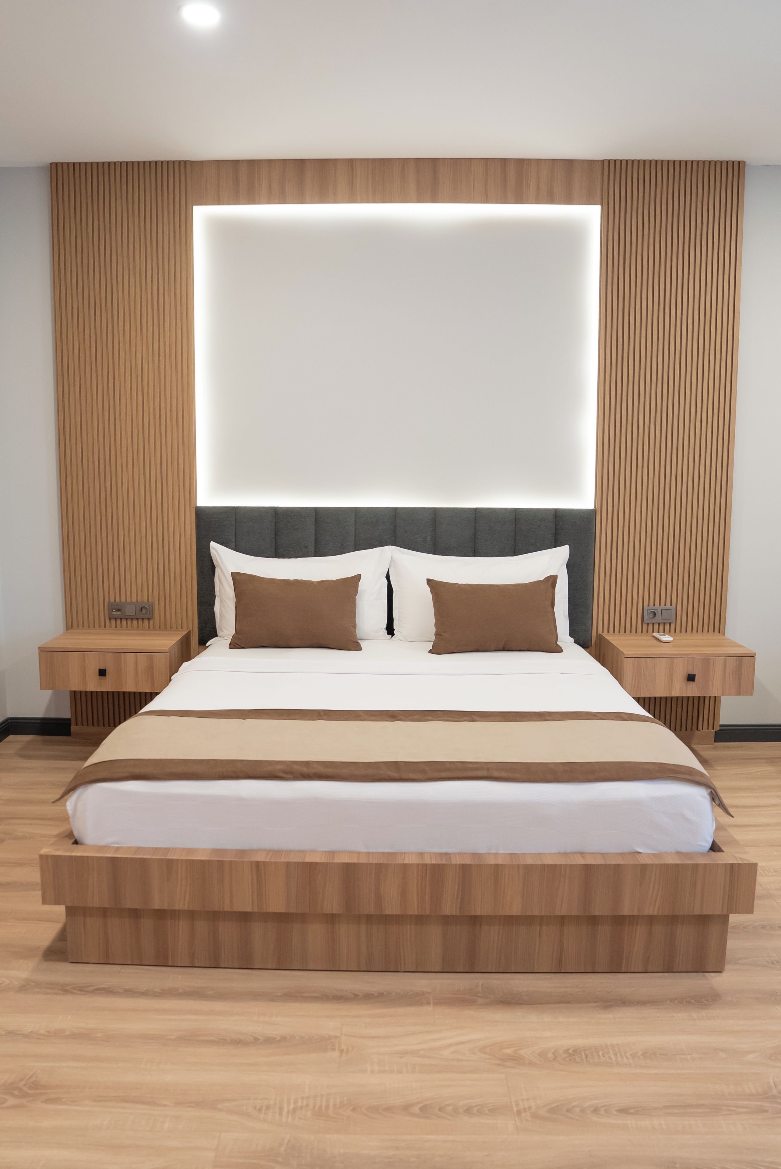 A modern bedroom with a large bed, wooden headboard, bedside tables, and a wall-mounted light.