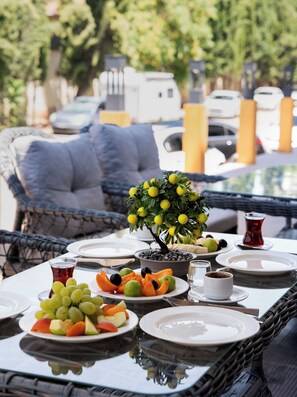 An outdoor dining area with wicker furniture, a table set with plates of fruit, a small tree, and a glass of red beverage. - Sever Suites Hotel (Antalya)