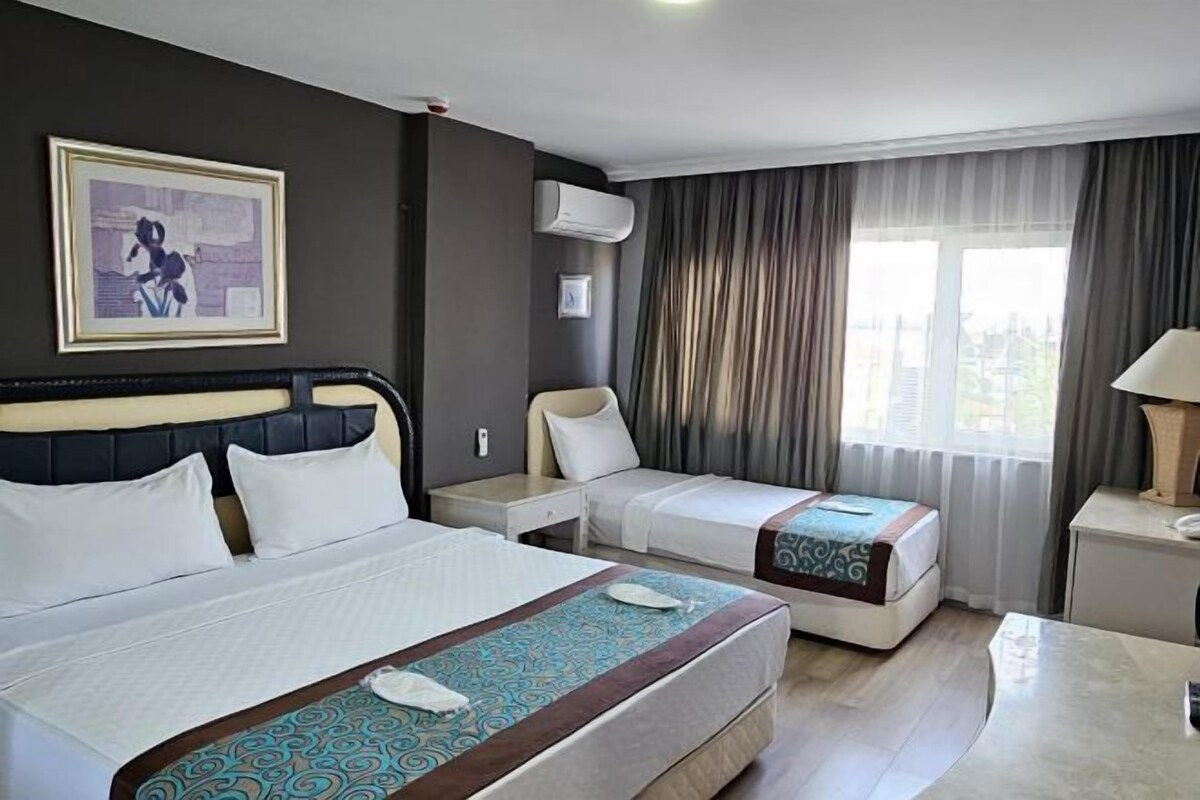 A hotel room with a large bed, a smaller bed, a desk, and a window with curtains.