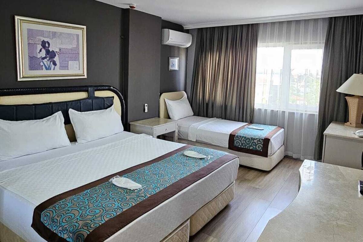 A hotel room with two beds, a desk, a chair, a window with curtains, and a painting on the wall.