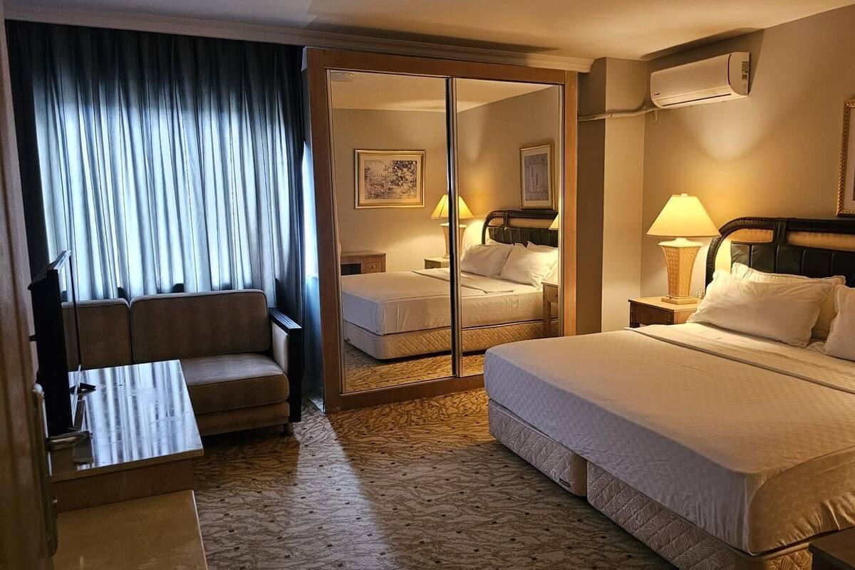A hotel room with a large bed, a sofa, a desk, and a mirror.