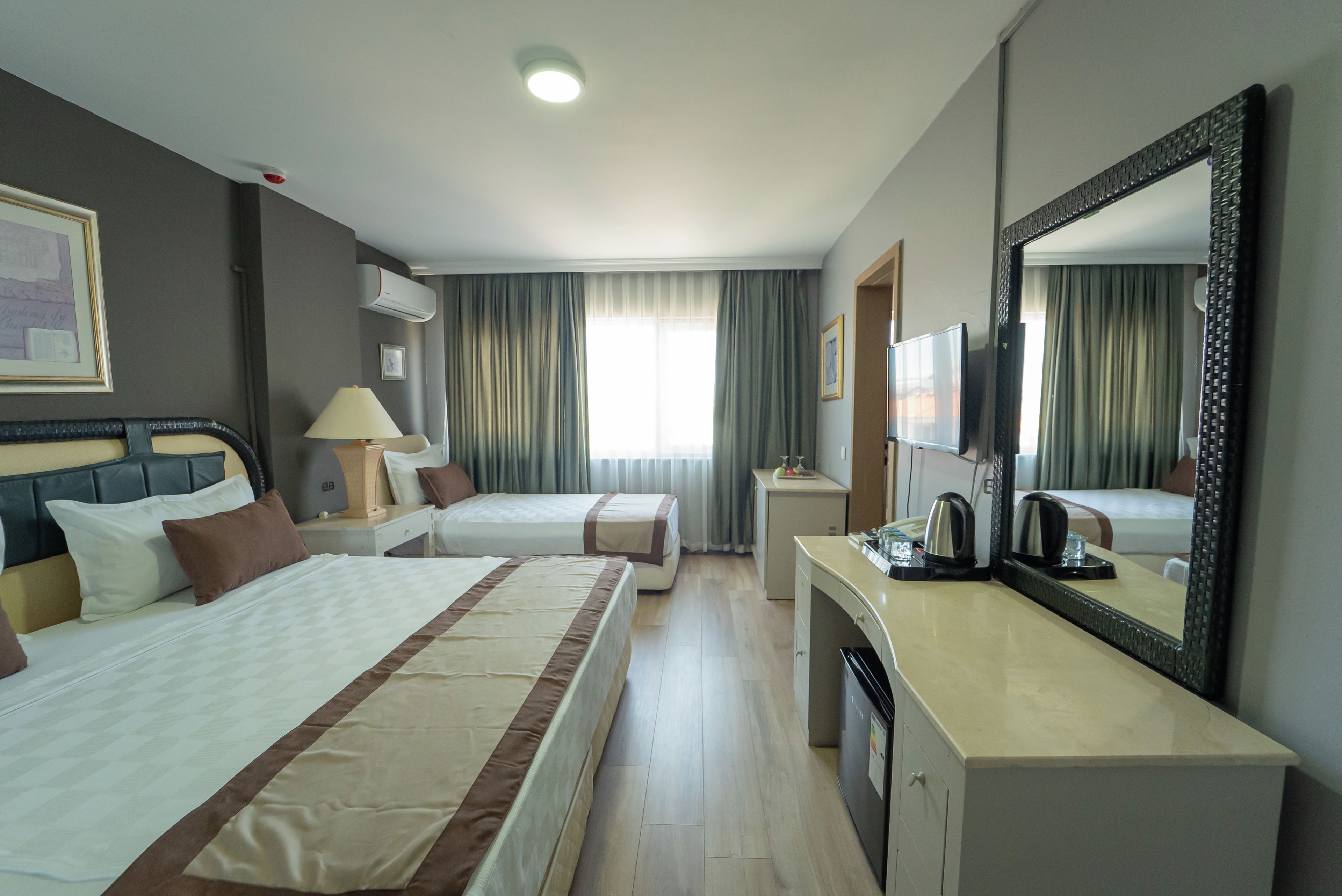 Ein Hotelzimmer mit zwei Betten, einem Schreibtisch, einem Spiegel und einem Fenster mit Vorhängen.