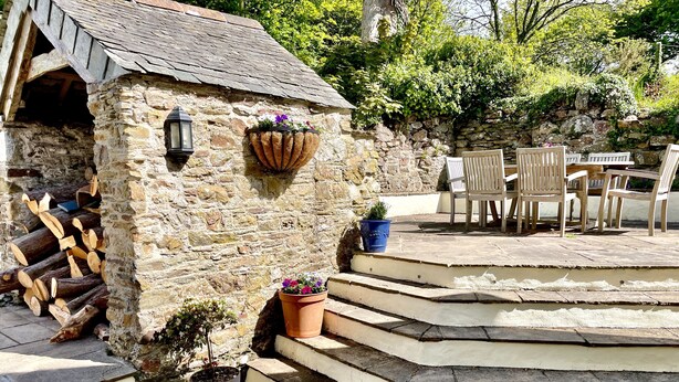 Un bâtiment en pierre avec un escalier en bois menant à un patio aménagé avec du mobilier d’extérieur.