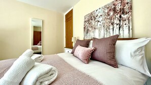 Une chambre d’hôtel avec un lit bien fait, un grand miroir, un tableau accroché au mur et une porte en bois.