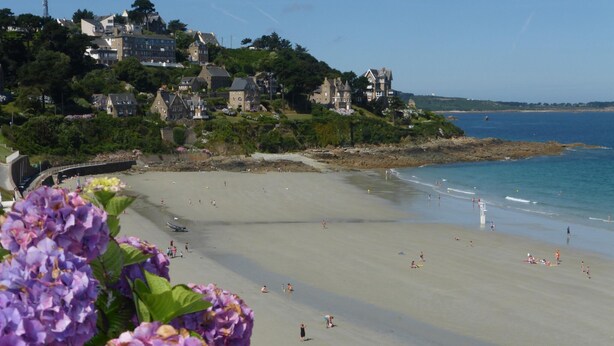 A beach with people swimming and sunbathing, houses on a hillside, and a clear sky. - Holiday Home in Guerlesquin near Lake (Guerlesquin)