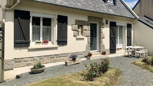 A house with a stone facade, a gravel driveway, and a small patio with a table and chairs. - Holiday Home in Guerlesquin near Lake (Guerlesquin)