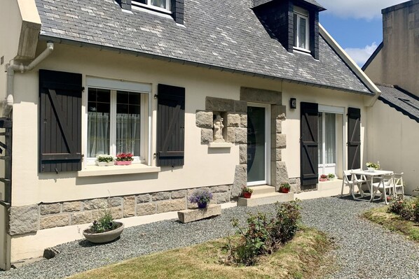 Ein Haus mit Naturstein-Fassade, einem Schotterweg und einer kleinen Terrasse mit Tisch und Stühlen.