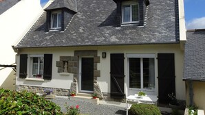A two-story house with a steeply pitched roof, stone foundation, and a small porch with a table and chairs. - Holiday Home in Guerlesquin near Lake (Guerlesquin)