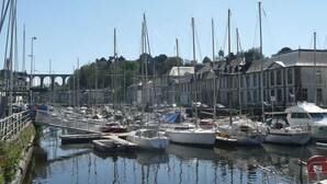 A marina with multiple boats docked, a bridge in the background, and buildings along the waterfront. - Holiday Home in Guerlesquin near Lake (Guerlesquin)