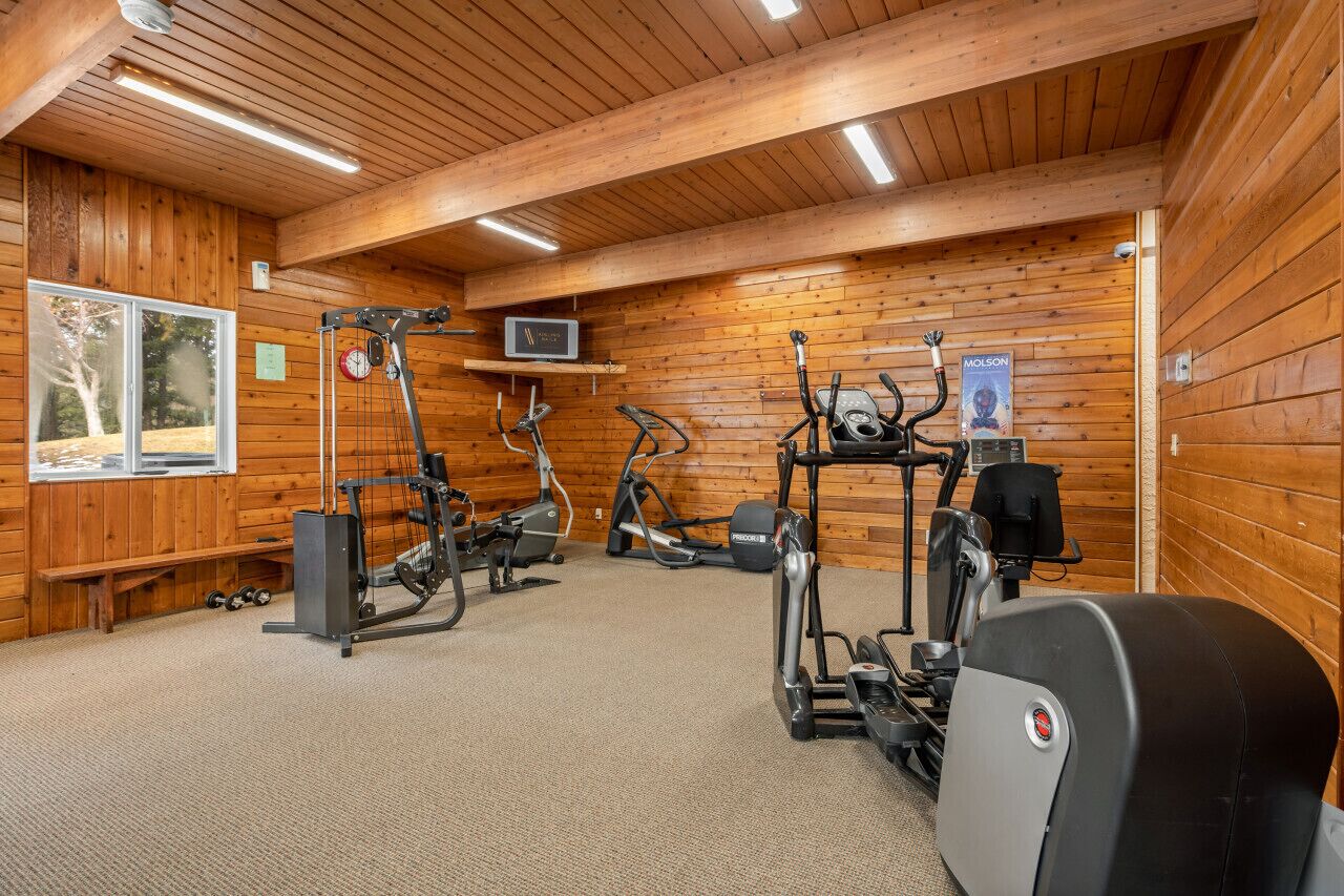 Ein Fitnessraum mit diversen Trainingsgeräten, Holzwänden und einer Decke mit freiliegenden Balken.