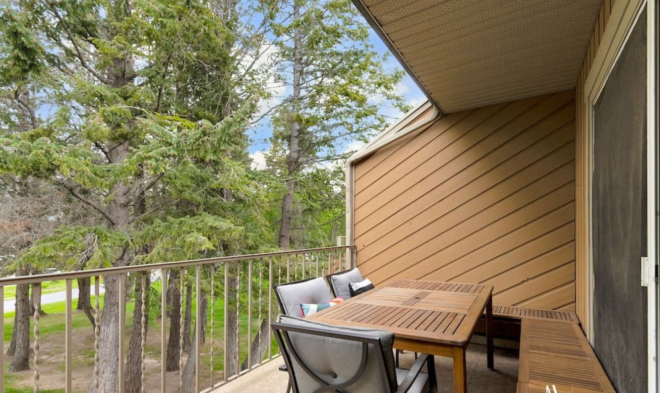 En balkon med et bord og stole, med udsigt over et skovområde.