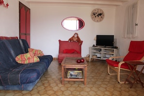 A living room with a sofa, a red chair, a small table, a television, and a bookshelf.