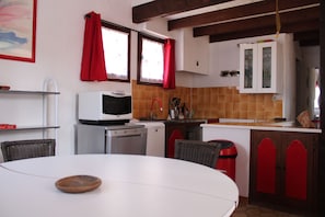 A kitchen with a white table, red cabinets, a microwave, and a dishwasher.