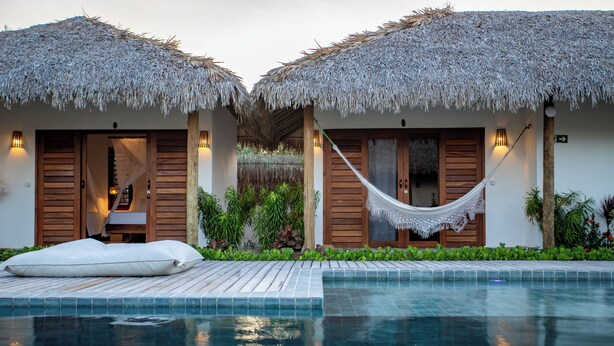 A pool area with two thatched-roof structures, each with a hammock and a bed. - Vilarejo Preá (Cruz)