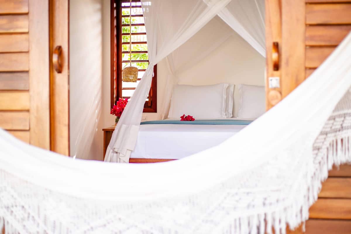 Una hamaca en una habitación con una cama, una ventana con cortinas y una puerta de madera.