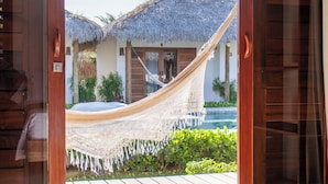 Una habitación con una cama grande, una puerta de madera y vistas a una estructura de techo de paja con piscina.