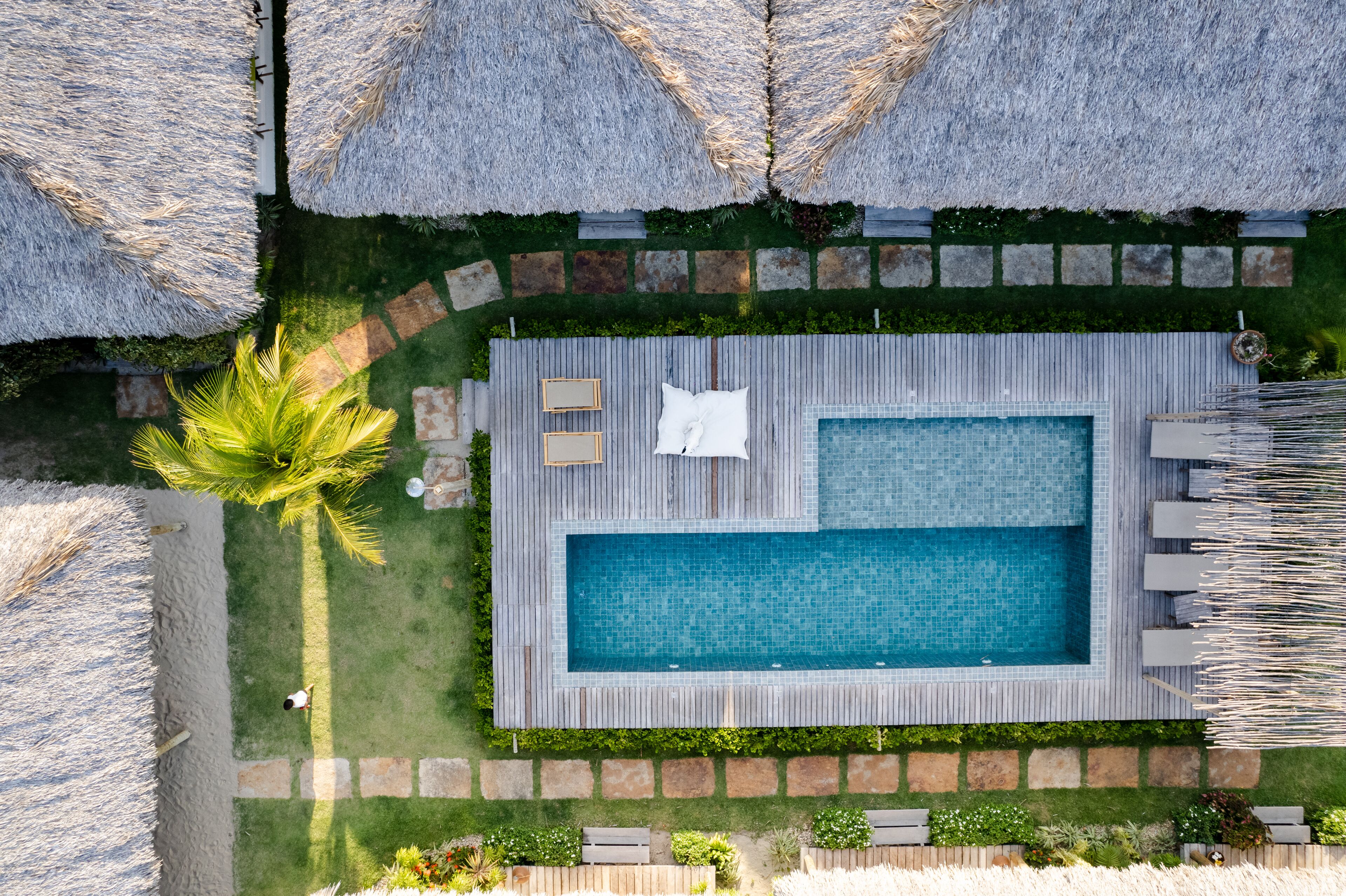 An aerial view of a swimming pool area with a wooden deck, lounge chairs, and a palm tree.